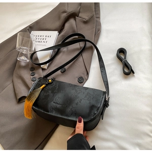 Detail of black shoulder bag with subtle bamboo patterns and yellow tassel on a suit