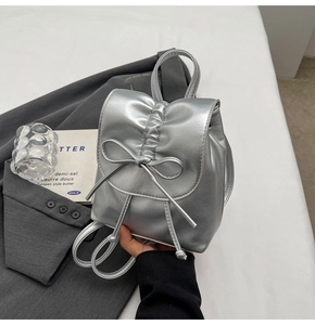 Détail du sac à dos plissé argenté avec nœud papillon sur fond de blazer gris