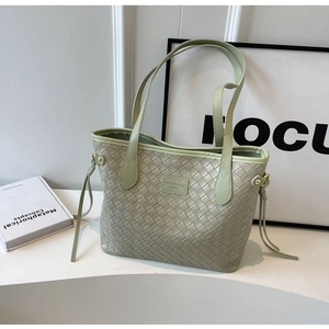 Close-up of light green woven tote bag with leather logo patch and shoulder straps