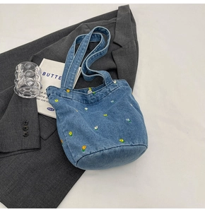 Detailansicht der Blumenstickerei auf blauer Denim-Tasche vor minimalistischem Hintergrund