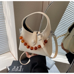 Detail view of cream white handbag with amber bead chain and textured leather finish