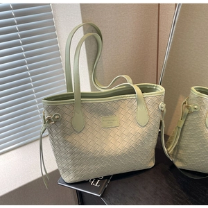 Detail of light green woven tote bag featuring dual straps and fashion trend logo patch