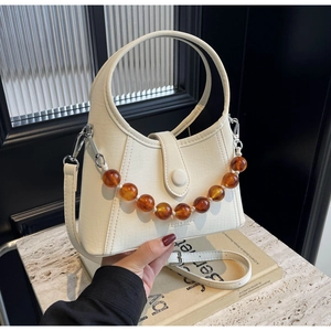 Detail of off-white leather handbag with amber beaded chain on marble surface