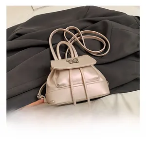 Detailansicht eines beigen Minirucksacks mit Metallschleife und Kordelzug auf grauem Stoff