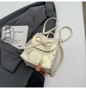 Détails d'un sac à dos crème plissé avec un nœud papillon et une texture PU nacrée