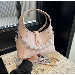 Detail of pink faux leather bag with pearl chain and gold branding on marble