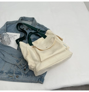 Detail of canvas tote bag showing green handles, adjustable strap and large front pocket
