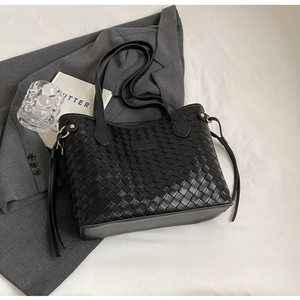 Detail of black woven tote bag with fringe accents and leather tag on office desk
