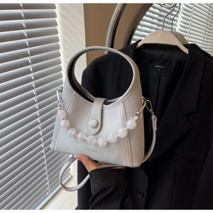 Detail of grey crossbody bucket bag featuring large decorative beads and silver hardware