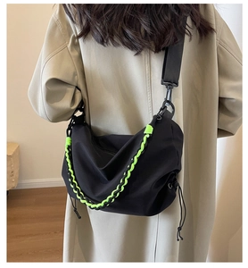 Detail of black nylon crossbody bag featuring a neon green woven chain and a stylish techwear look