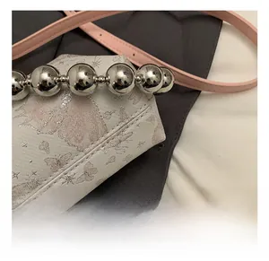 Detail showing silver sphere hardware and butterfly embroidery on the white bag