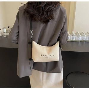 Détail du sac à main minimaliste en toile crème montrant l'imprimé texte et la fine bandoulière