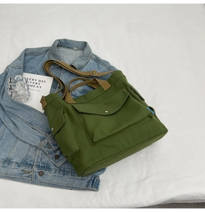 Detail of green canvas tote bag featuring brown straps and functional front flap pocket