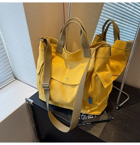 Detail of yellow canvas tote bag featuring front snap pocket and adjustable wide strap