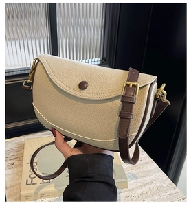 Detail of cream lychee leather saddle bag with brown trim and gold metallic hardware