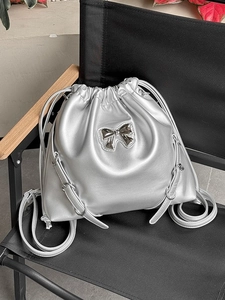 Metallic silver drawstring bucket backpack with bow detail on a black chair