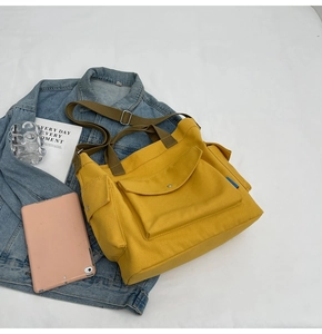 Overhead view of yellow canvas tote bag with brown handles, pockets, and daily essentials