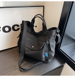 Detail of black canvas tote bag showing front flap pocket with snap and side storage pocket
