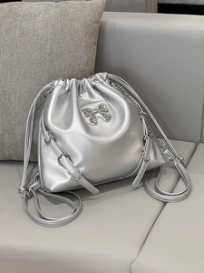 Silver metallic drawstring bucket backpack with bow detail and chain straps on a sofa