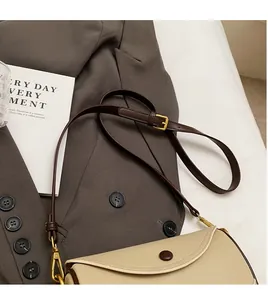 Close-up of beige lychee leather saddle bag with brown trim and gold buckle details