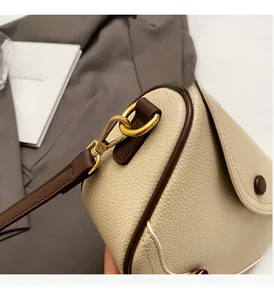 Close-up of premium golden metal hook on an off-white pebble leather saddle bag