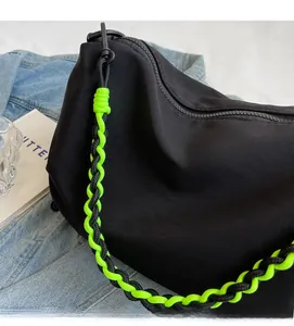 Detail of black crossbody bag featuring a green and black braided rope strap and matte metal hook