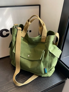Green canvas tote bag with khaki straps and multiple pockets in a 45-degree side view