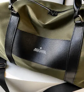 Detail of olive green nylon travel bag featuring black leather trim and zipper texture