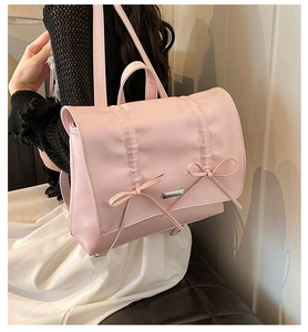 Side view of a pink bow backpack in PU leather worn by a model in a minimalist setting