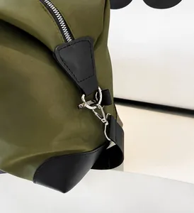 Close-up of military green nylon travel bag featuring silver metal hooks and black leather trim