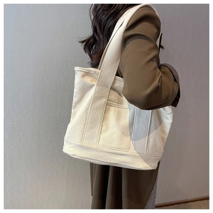Model wearing a large cream canvas tote bag showing its size and casual style on a gray wall
