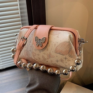 Pink crossbody bag with butterfly embroidery and silver beaded handle on warm background