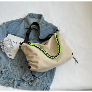 Detail of beige nylon crossbody bag featuring neon green woven handle and drawstring