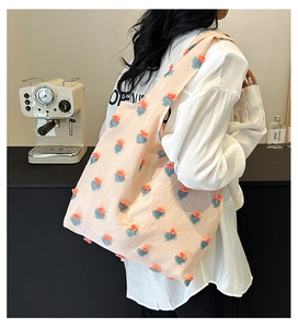 Detail of light pink tote bag featuring 3D floral pom-poms and wide shoulder strap