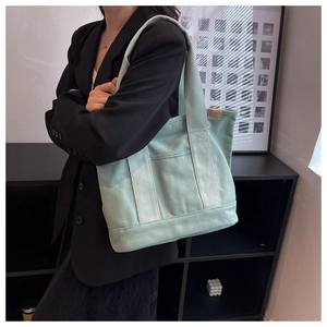 Detail view of mint green canvas tote bag with wide handles and leather patchwork accents
