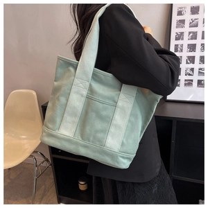 Detail of light green canvas tote bag showing wide shoulder strap and side pocket
