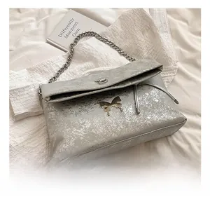 Detail view of silver-grey textured flap bag featuring a vintage metal butterfly clasp