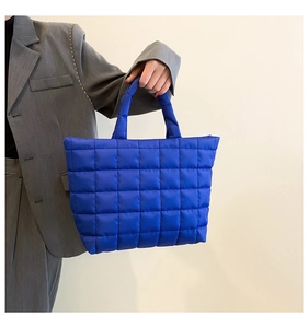 Detailed view of the bright blue quilted tote bag held by a model in a grey suit