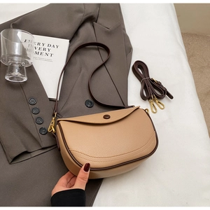Detail of khaki pebbled leather saddle bag with dual straps and retro gold hardware