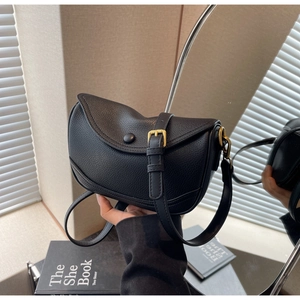 Detailed view of black lychee grain leather saddle bag with round buckle and golden hardware