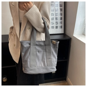 Detail of grey canvas tote bag featuring comfortable wide straps and front slip pocket