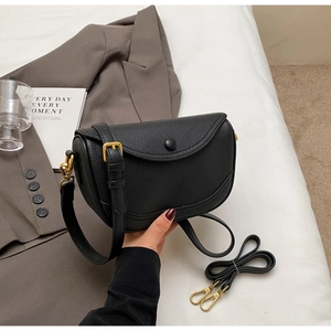 Detail of black lychee grain leather saddle bag with gold hardware and dual straps