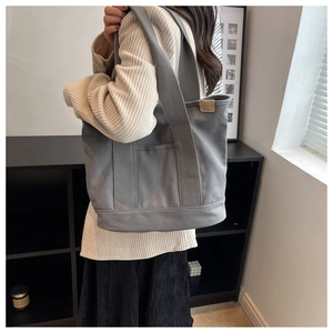 Detailed view of gray canvas tote bag with wide straps worn by a model in a modern room