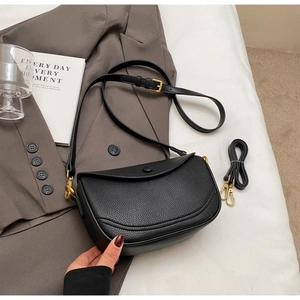 Detail of black lychee grain leather saddle bag with gold hardware on grey suit