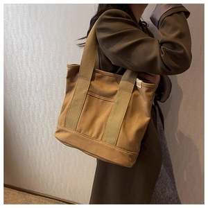 Close-up of tan canvas tote bag featuring wide strap and front pocket detail
