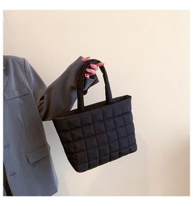 Detail of black quilted tote bag showing a textured puffer pattern and nylon top handles