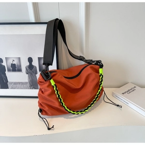 Detail of orange nylon shoulder bag with drawstring base and vibrant neon yellow woven cord