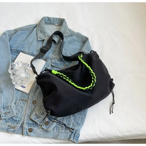 Detail of black nylon dumpling bag with neon green woven handle on denim jacket