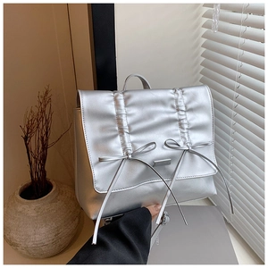 Detail of silver pleated backpack featuring delicate bows and long tassel accents
