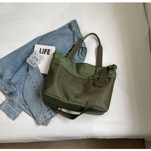 Detail of olive green canvas and mesh tote bag with adjustable shoulder strap on white bed